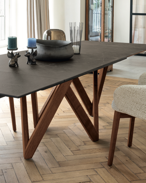 Contemporary dining table with a dark stone top and distinctive wooden V-shaped legs, showcasing modern furniture design from Calligaris.