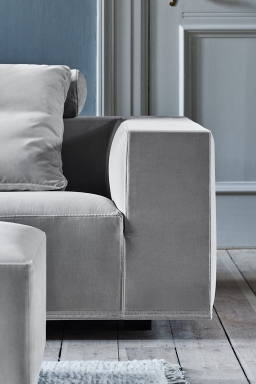 A modern, light gray upholstered sofa with clean lines and a plush pillow, situated in a stylish living room with wooden flooring and a white rug.