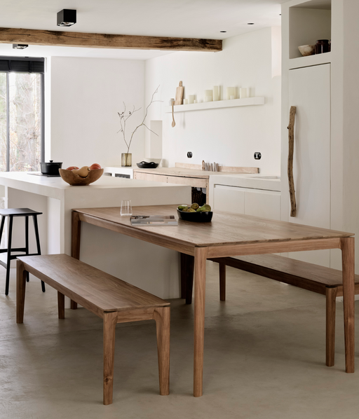 Minimalist kitchen interior featuring natural wood dining table and benches, with white cabinetry and decorative accents, showcasing Ethnicraft joins the Trade Source Furniture Collection.