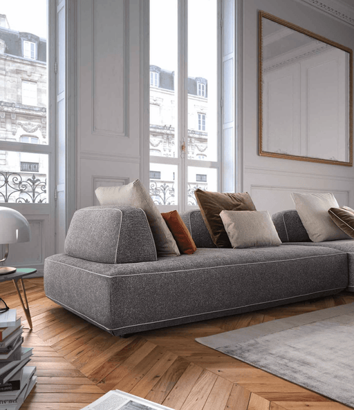 Elegant contemporary living room with a plush gray sofa, assorted throw pillows, large windows with Parisian architecture, and classic white wall paneling.