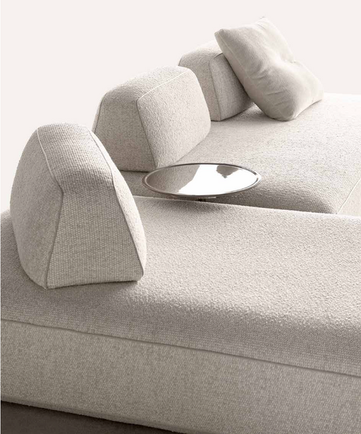 Minimalist beige sofa with movable backrests and matching cushions, designed for open interior spaces and flexible seating arrangements.