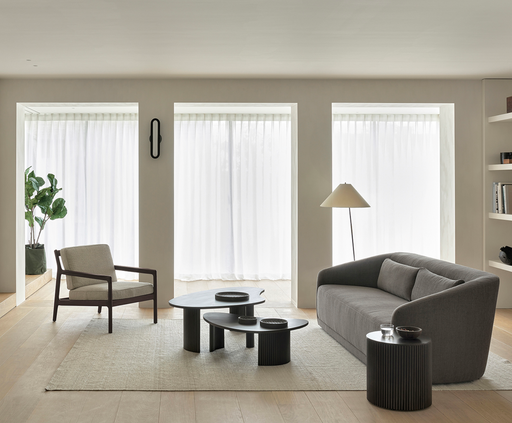 A modern minimalist living room featuring neutral tones, sleek black coffee tables, a gray sofa, a beige armchair, and large windows with sheer white curtains, embodying contemporary interior design trends focused on elegance and innovation.