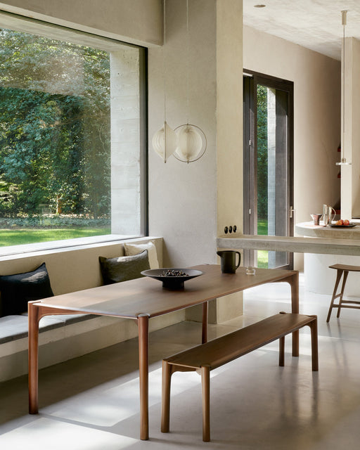 A modern dining area featuring solid wood furniture with natural finishes, minimalist design, and large windows showcasing lush outdoor greenery.