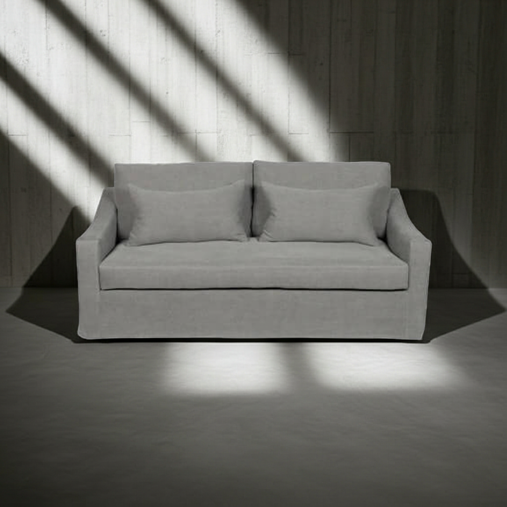 Gray sofa with two cushions in a room with light filtering through a window.