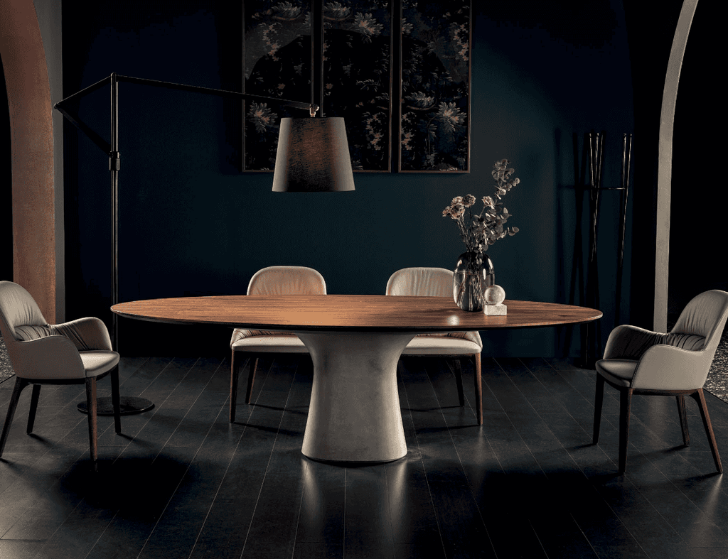 Elegant oval dining table with a warm wooden surface and a rounded concrete pedestal base, set in a dark-themed room with beige chairs and minimalist decor