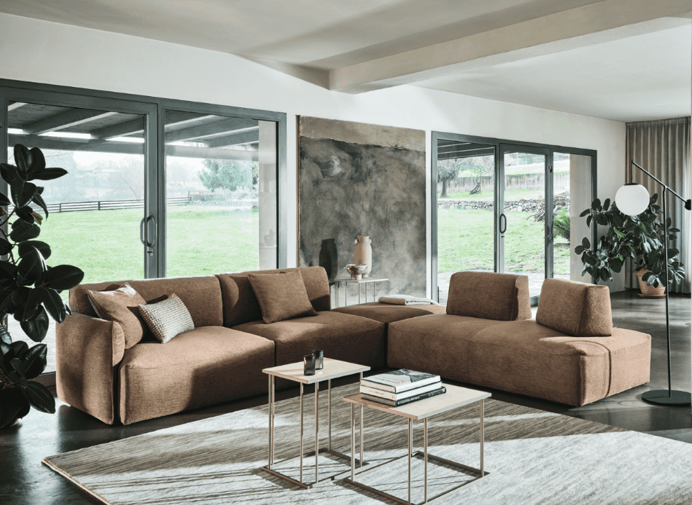 Spacious living room with large beige sectional sofa, neutral decor, and natural light from floor-to-ceiling windows overlooking outdoor landscape