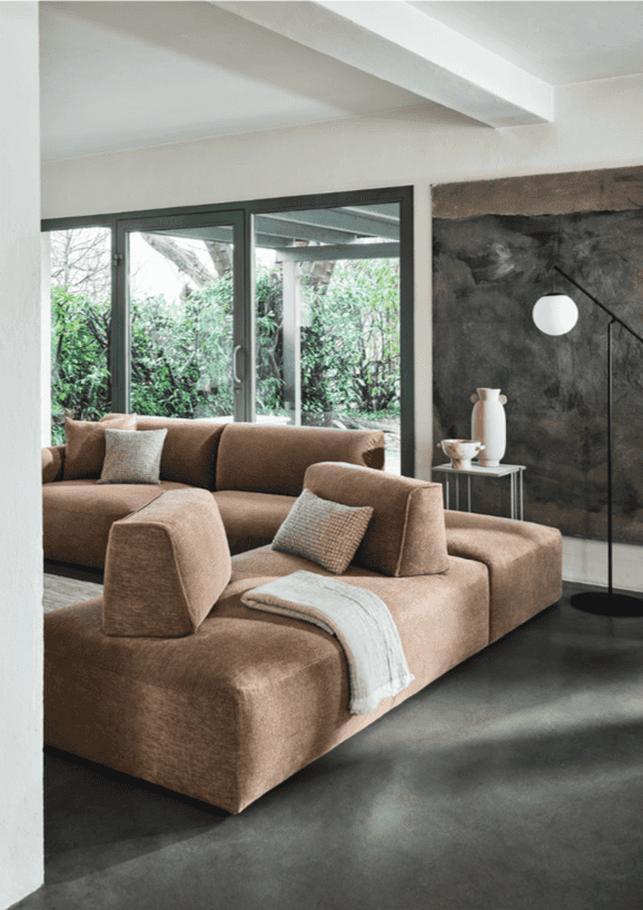 Living room with large beige sectional sofa with adjustable backrests, soft cushions, and a modern minimalist design, near glass doors opening to greenery