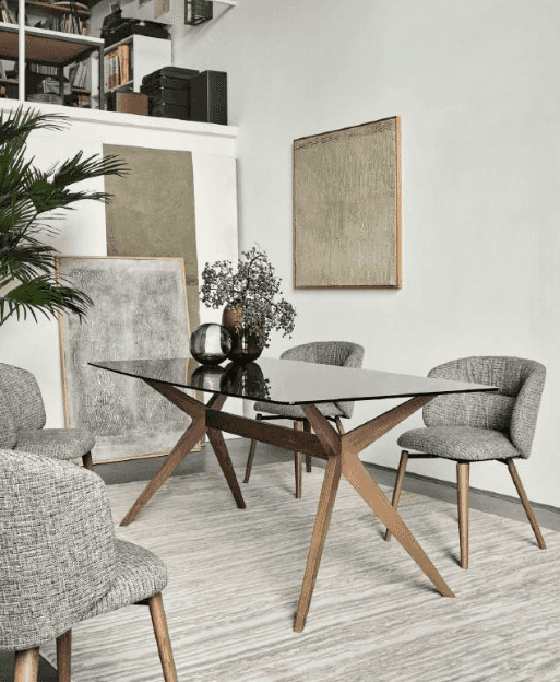 Elegant dining table with a glass surface and wooden legs, surrounded by chairs in a modern interior with artwork on the wall.
