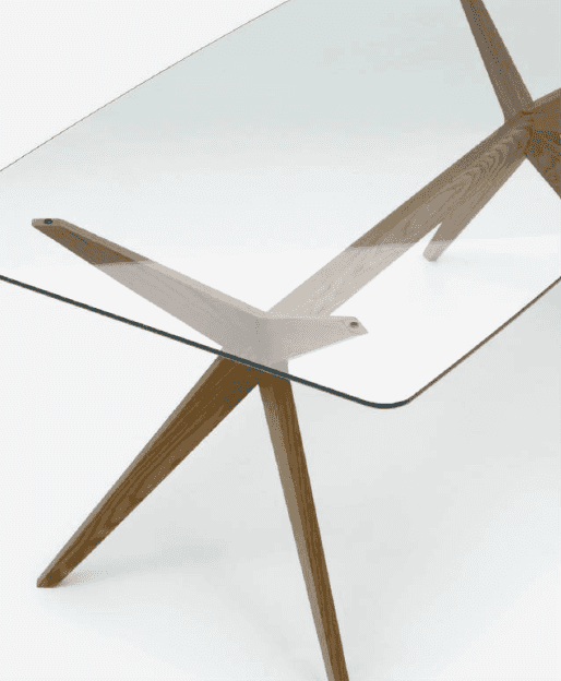 Close-up of a modern dining table with a clear glass top and wooden angled legs, showcasing sleek contemporary design.