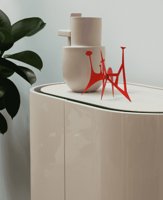 Modern white storage cabinet with a glossy finish, rounded edges, and black legs, topped with decorative ceramic vases and a red abstract sculpture