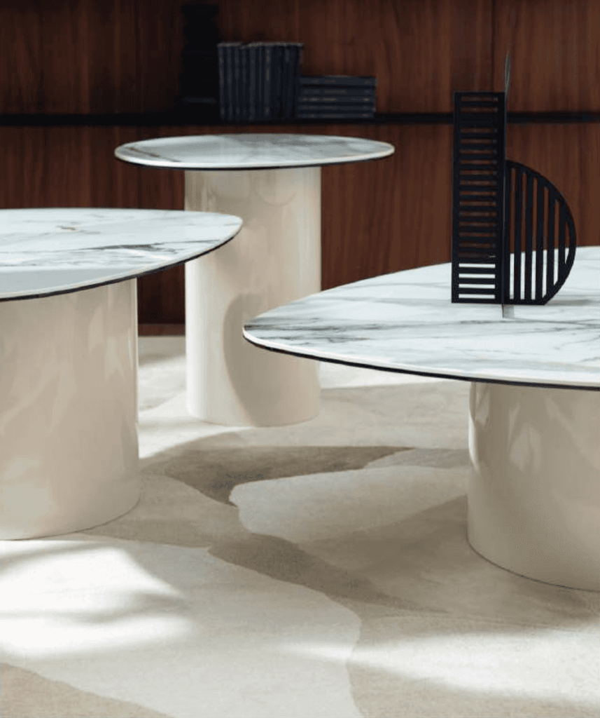 Set of modern accent tables with round marble tops and sculptural cream-colored bases, featuring a black decorative partition on one table, ideal for contemporary living spaces.