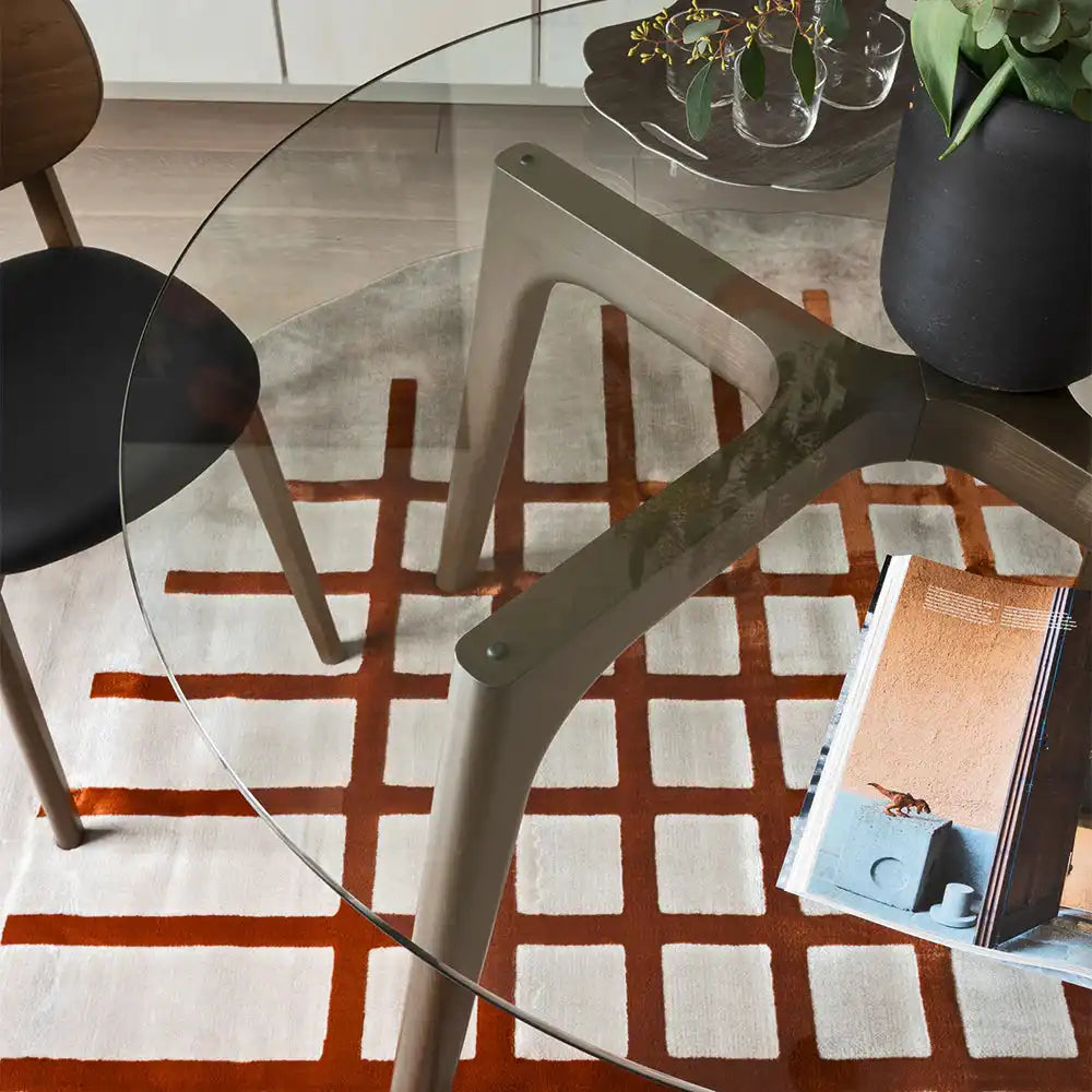 Round glass dining table with sleek metal legs in a modern dining room, decorated with a black vase and green plants