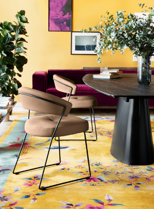 Contemporary beige dining chair with cushioned seat and backrest, black metal frame, placed in a colorful living room setting