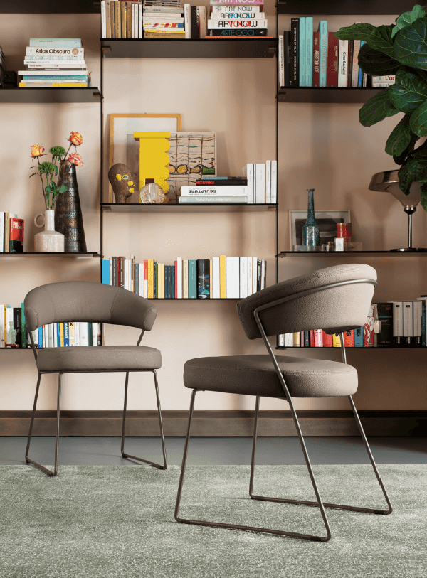 Modern gray upholstered chairs with slim black metal legs, set against a bookshelf wall in a cozy home library