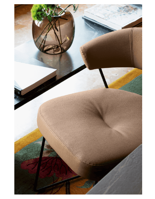 Close-up of a beige lounge chair with cushioned seat and backrest, black metal frame, on a colorful patterned rug