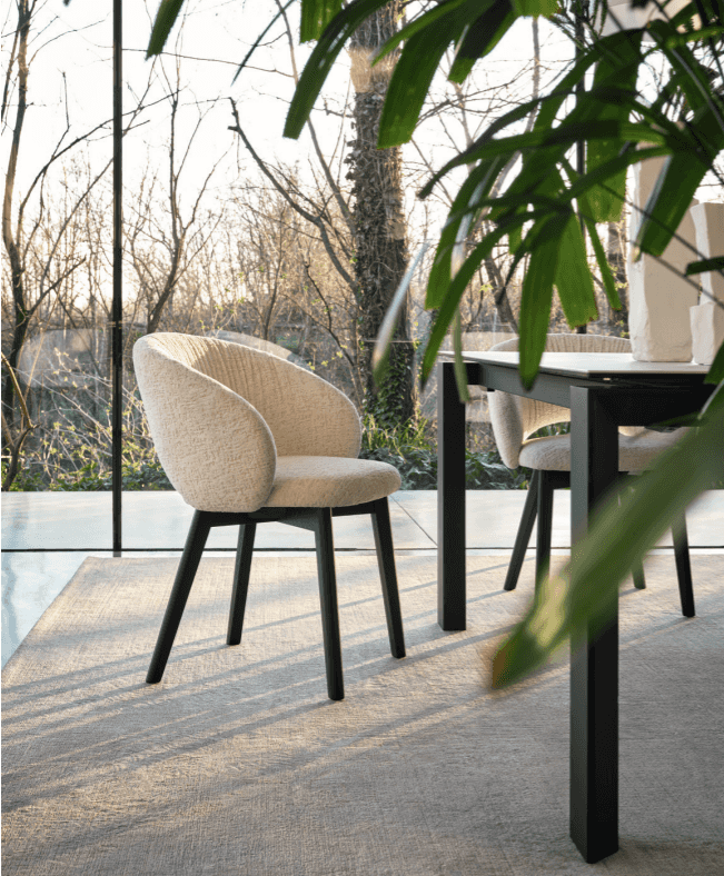 Stylish dining room with a black table and cream upholstered chairs with black legs, overlooking a scenic outdoor view.