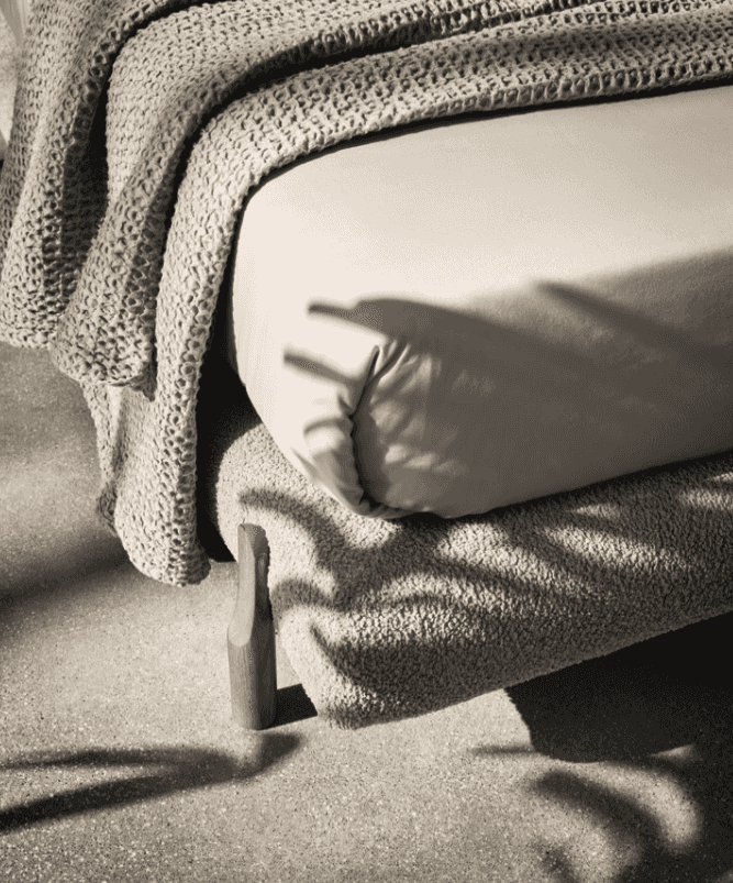 Corner detail of the CS6218 Oleandro Bed by Calligaris Italy showing boucle fabric and wooden leg, bathed in natural light with a cozy knit throw.