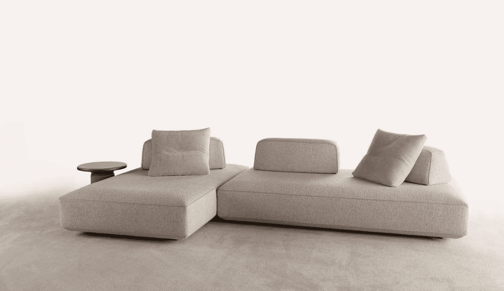Modern living room featuring a large, light-colored sofa with multiple cushions, set against elegant white walls and wooden flooring