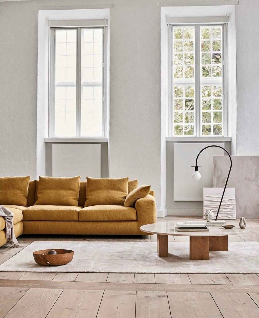Aton Sofa by Eilersen in mustard yellow fabric, styled in a minimalist living room with tall windows, available at Trade Source Furniture.
