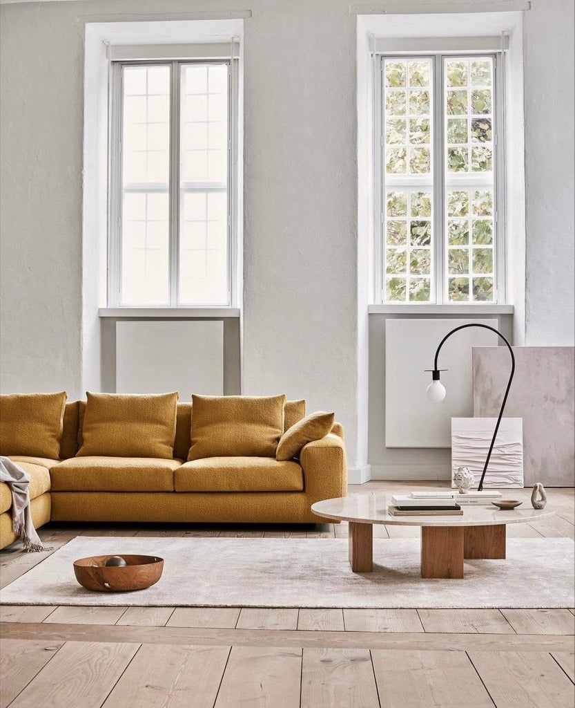 Aton Sofa by Eilersen in mustard yellow fabric, styled in a minimalist living room with tall windows, available at Trade Source Furniture.