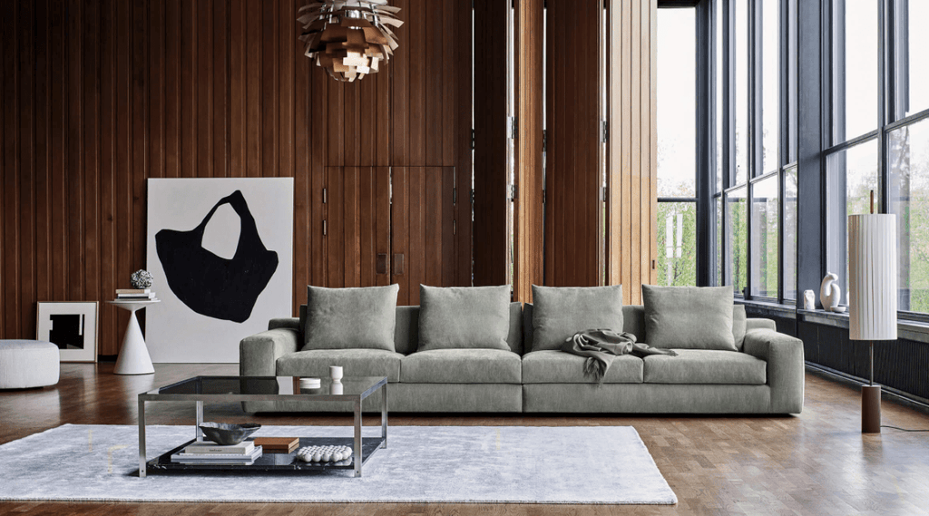 Extra-long Aton Sofa by Eilersen in sage green fabric, styled in a modern wood-paneled room, available at Trade Source Furniture.