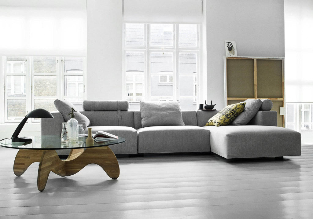 Modern living room with Eilersen Baseline Sofa with Chaise in grey, paired with a sculptural wood coffee table and floor-to-ceiling windows.