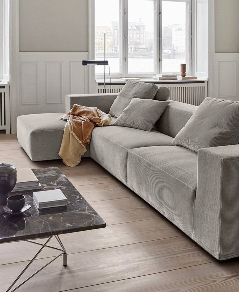 Quick Ship Baseline Sofa with Chaise by Eilersen in light grey fabric, styled in a modern Scandinavian living room with wood flooring and large windows.