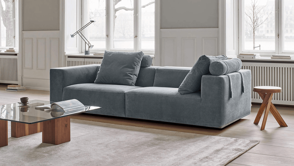 Compact version of the Eilersen Baseline Sofa with Chaise in blue-grey fabric, styled in a Scandinavian room with wood accents.