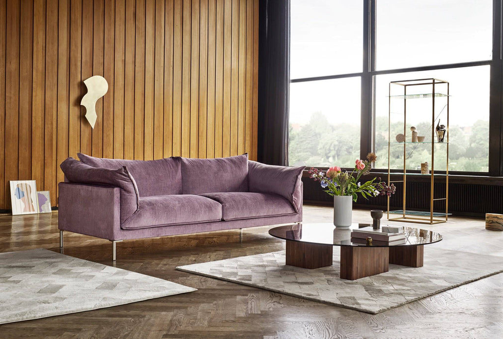 Butterfly Sofa by Eilersen in lavender fabric set in a wood-paneled room with large windows, blending formal design with cozy ambiance.