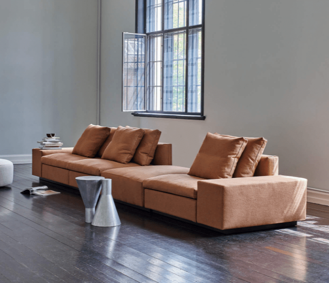 The Dacapo Sectional Sofa by Eilersen in brown fabric, shown in a modern living room with wood floors and large windows, available at Trade Source Furniture.
