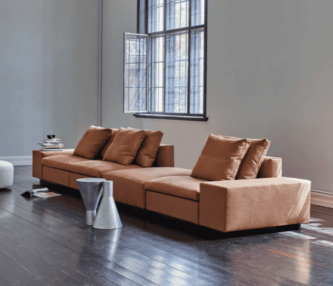 The Dacapo Sectional Sofa by Eilersen in brown fabric, shown in a modern living room with wood floors and large windows, available at Trade Source Furniture.