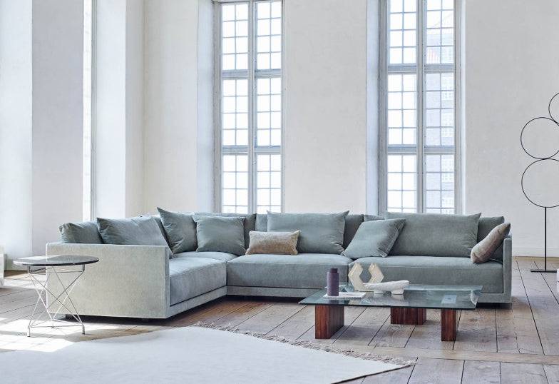 Drop Sectional Sofa in soft blue fabric by Eilersen, placed in a bright room with tall windows and modern decor elements.