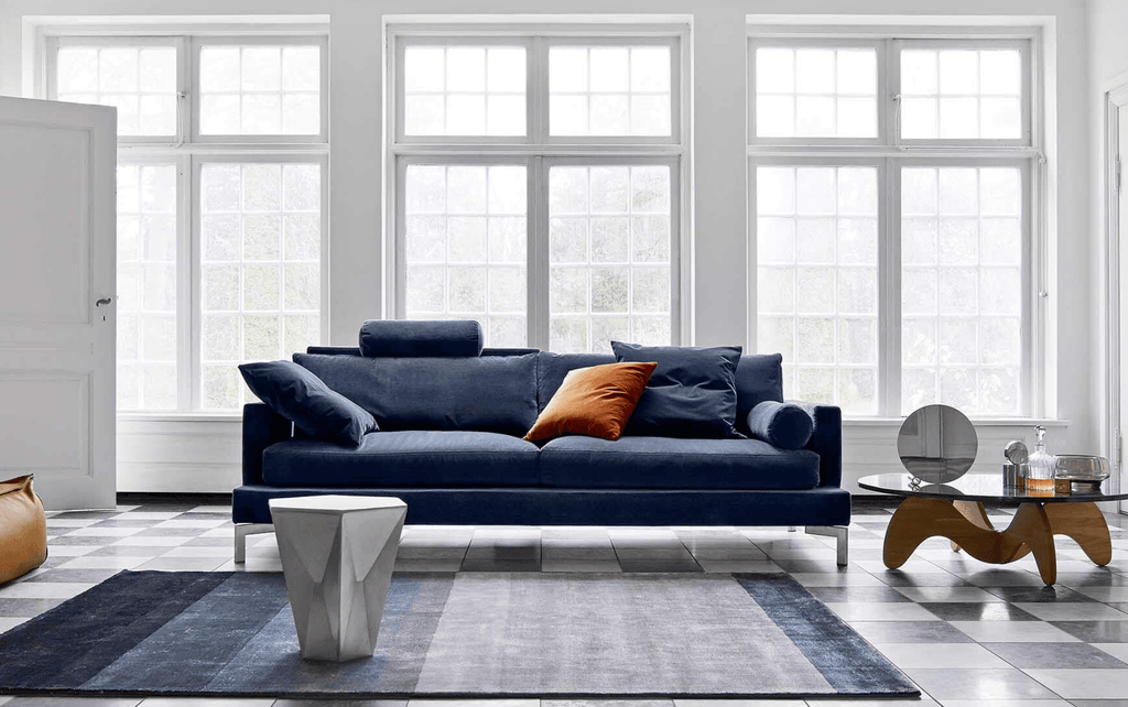The Great Lift Sofa by Eilersen at Trade Source Furniture in navy blue, styled with colorful pillows in a bright, windowed living space.