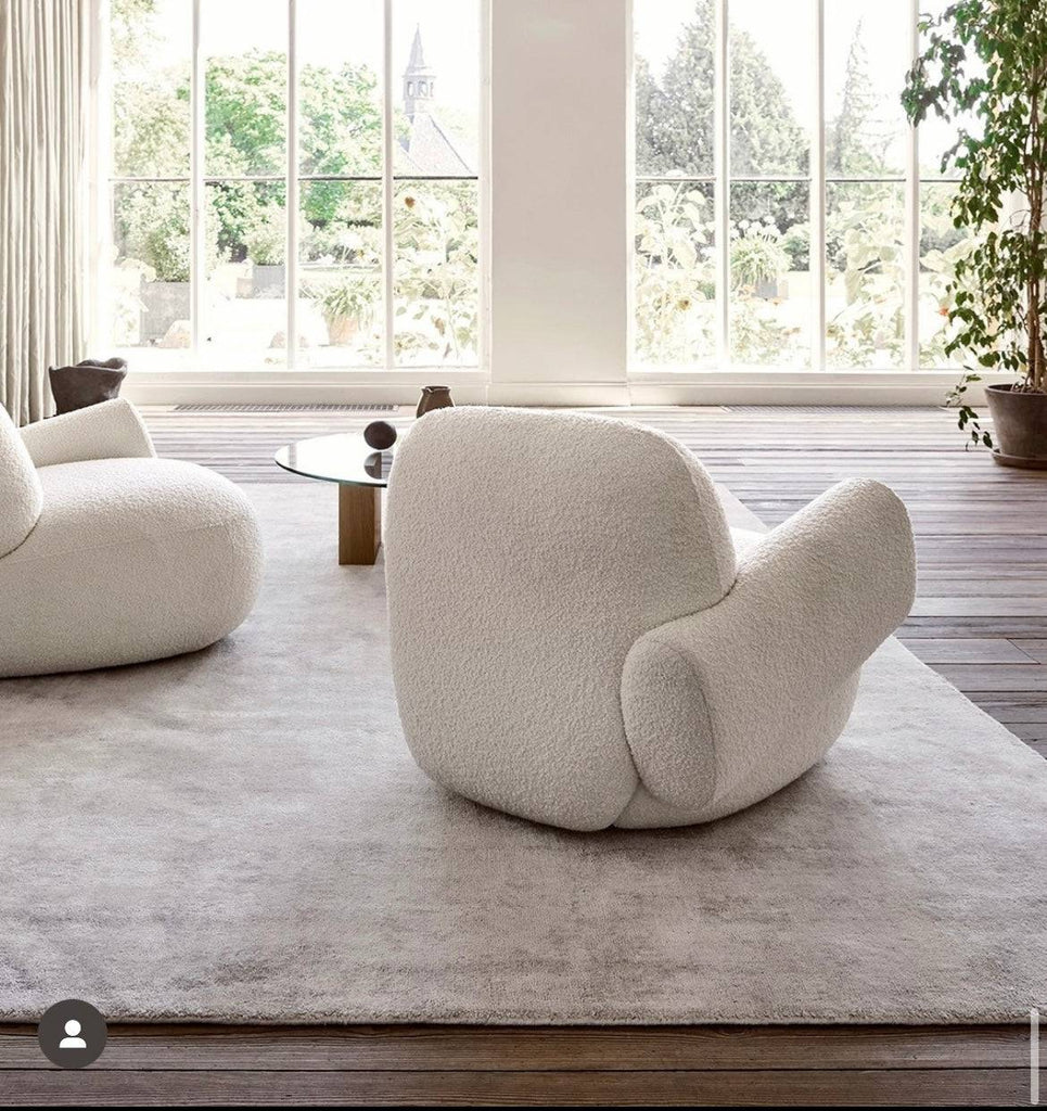 Back view of two Havana Round Arm Chairs by Eilersen in white boucle, placed in a sunlit room with large windows and a soft rug.