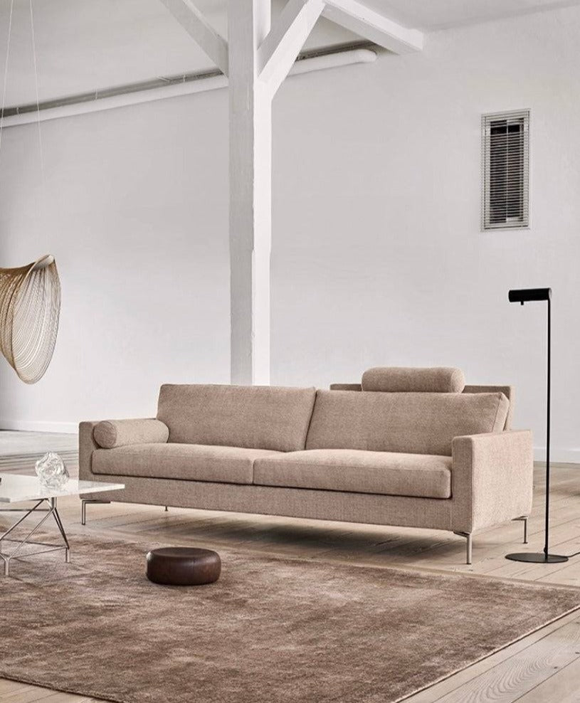 Quick Ship Lift Sofa by Eilersen in beige fabric with headrest and cylindrical pillow, set in a modern minimalist living room with neutral tones.