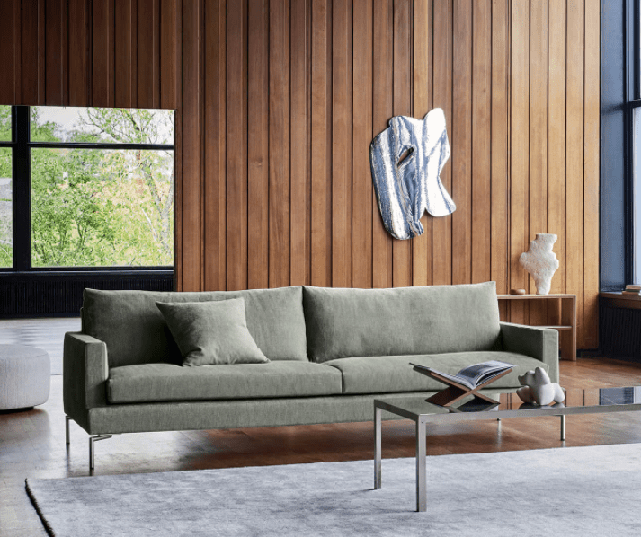 Loft Sofa by Eilersen in sage green fabric displayed in a modern wood-paneled living room at Trade Source Furniture. Ideal for contemporary interiors.