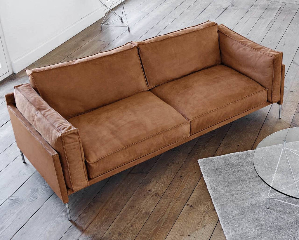 Slimline Sofa by Eilersen in warm brown leather finish, featuring slim metal legs and plush cushions on wooden flooring.