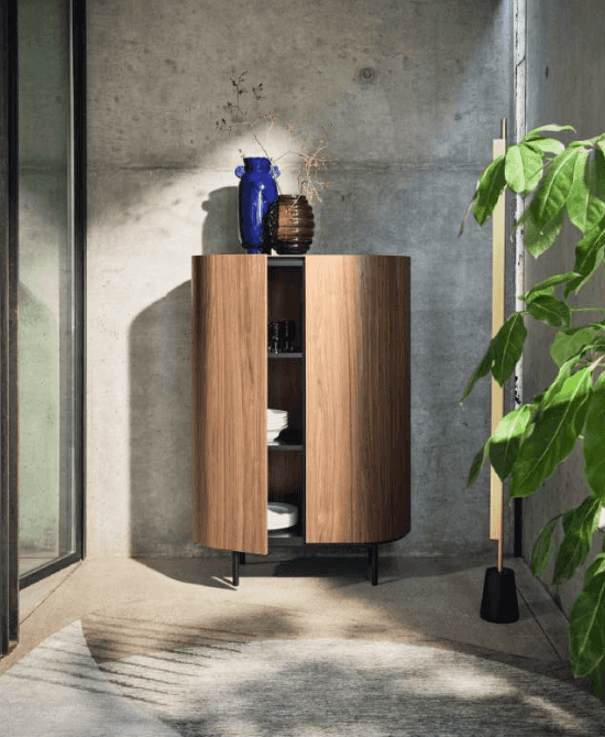 Wooden Lake Bar Cabinet with curved doors, open shelving inside, black metal legs, decorated with vases and flowers in modern interior