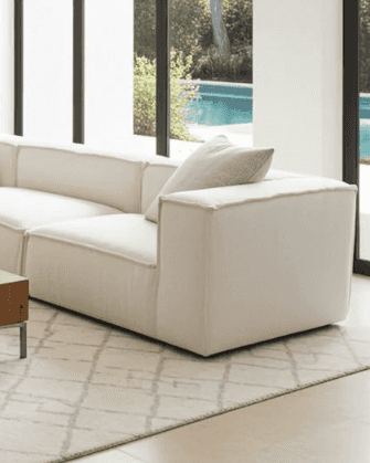 Elegant living room with a white sectional sofa, large glass doors, and a view of the outdoor pool and lush landscape