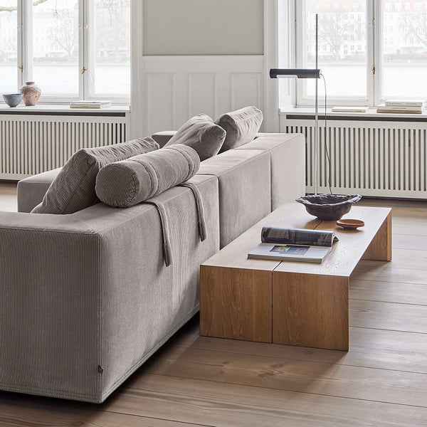 Rear view of the Eilersen Baseline Sofa with Chaise in grey corduroy, featuring a head roll and styled with a low wood console table.