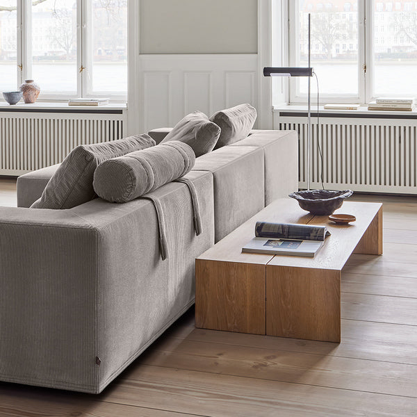 Rear view of the Eilersen Baseline Sofa with Chaise in grey corduroy, featuring a head roll and styled with a low wood console table.