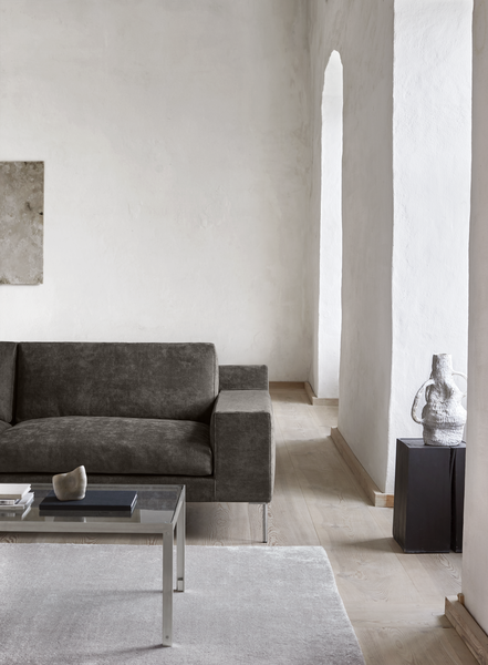 Side view of Shu Sofa by Eilersen in grey fabric, paired with a glass coffee table in a minimalist interior setting with soft lighting.