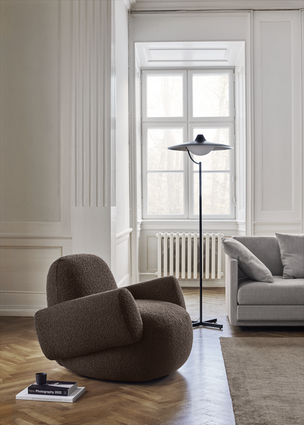 Sunlit room with Havana Round Arm Chair by Eilersen in dark boucle, styled beside a modern glass coffee table.