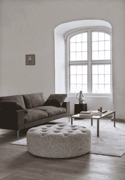 Shu Sofa by Eilersen in a cozy corner with a round tufted ottoman and modern decor, ideal for stylish and comfortable living rooms.