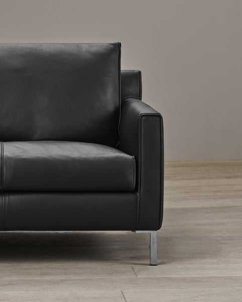 Close-up of the Streamline Sofa by Eilersen at Trade Source Furniture in black leather, focusing on armrest stitching and chrome leg detail.