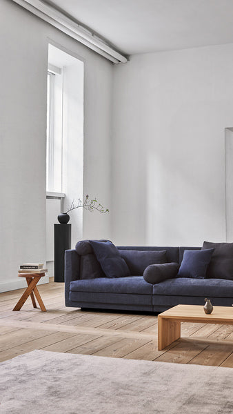 Cocoon Sofa by Eilersen at Trade Source Furniture in deep blue fabric, placed in a minimalist room with wood flooring and modern decor.