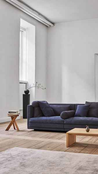 Cocoon Sofa by Eilersen at Trade Source Furniture in deep blue fabric, placed in a minimalist room with wood flooring and modern decor.