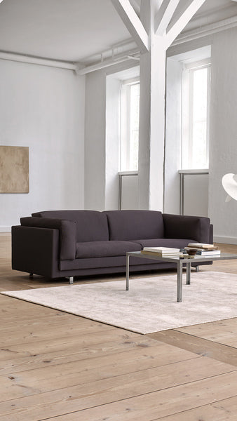 Eilersen Tub Sofa in dark fabric placed on a light rug in a bright, open living space with high ceilings and modern decor.