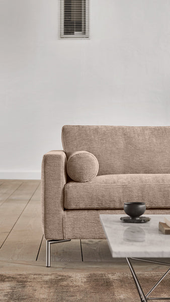 Close-up of beige Quick Ship Lift Sofa by Eilersen armrest and round pillow, showcasing textured upholstery and sleek metal legs.