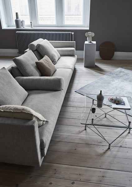 Cocoon Sofa by Eilersen at Trade Source Furniture in a spacious living room, styled in grey fabric with multiple cushions and a glass coffee table.
